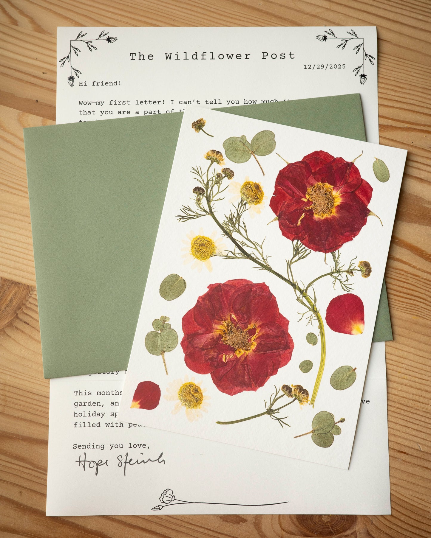 The Wildflower post letter with with a dark green envelope and fine art print of a pressed rose and chamomile.
