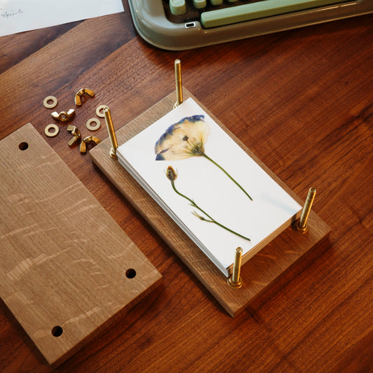 Wood flower press with brass bolts with the top off showing a pressed flower.
