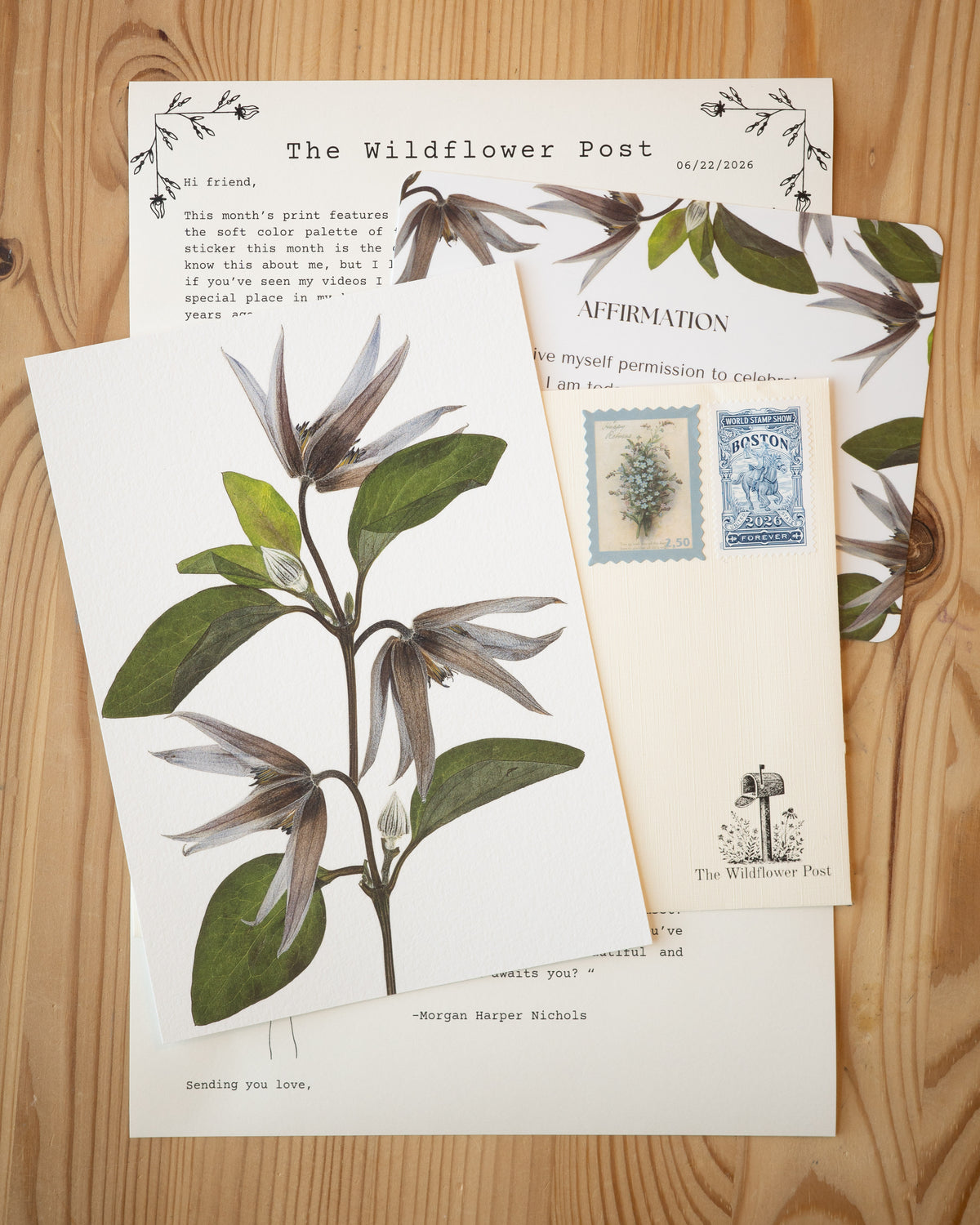 Art print of pressed clematis with letter and affirmation card on table.