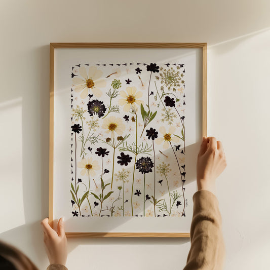 Person hanging a framed print of floral pressed flower collage art print design on a wall