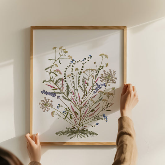 Person hanging a framed botanical pressed flower art print on a wall.