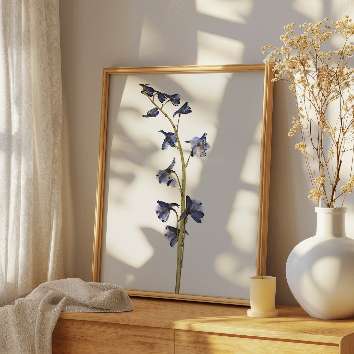 Framed artwork of pressed flower art print on a wooden surface with a white vase containing dried yellow flowers.