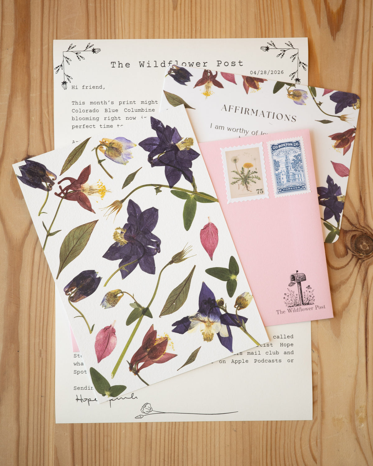 Art print of pressed columbine with letter and affirmation card on table.