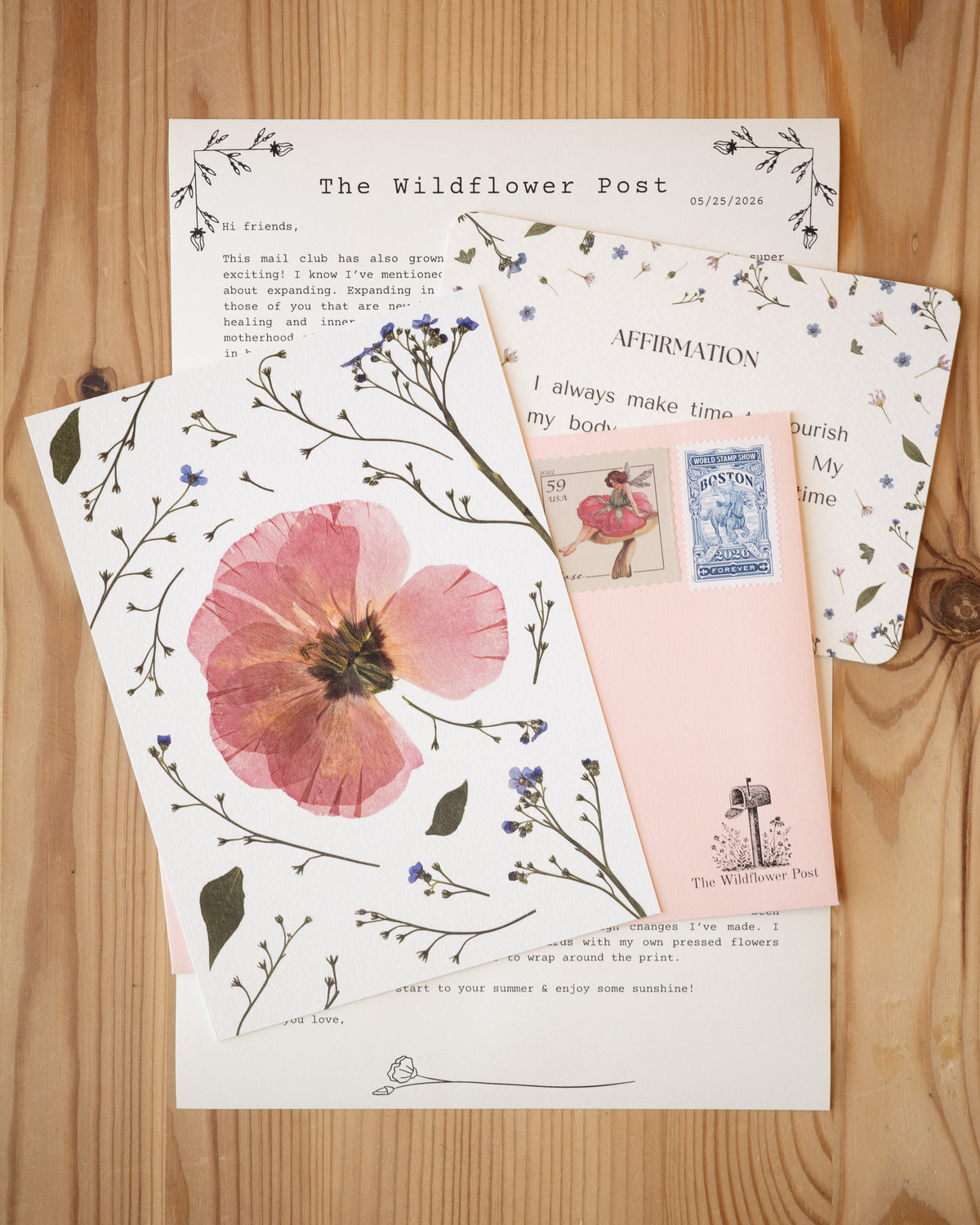 Art print of pressed pink lisianthus with letter and affirmation card on table.
