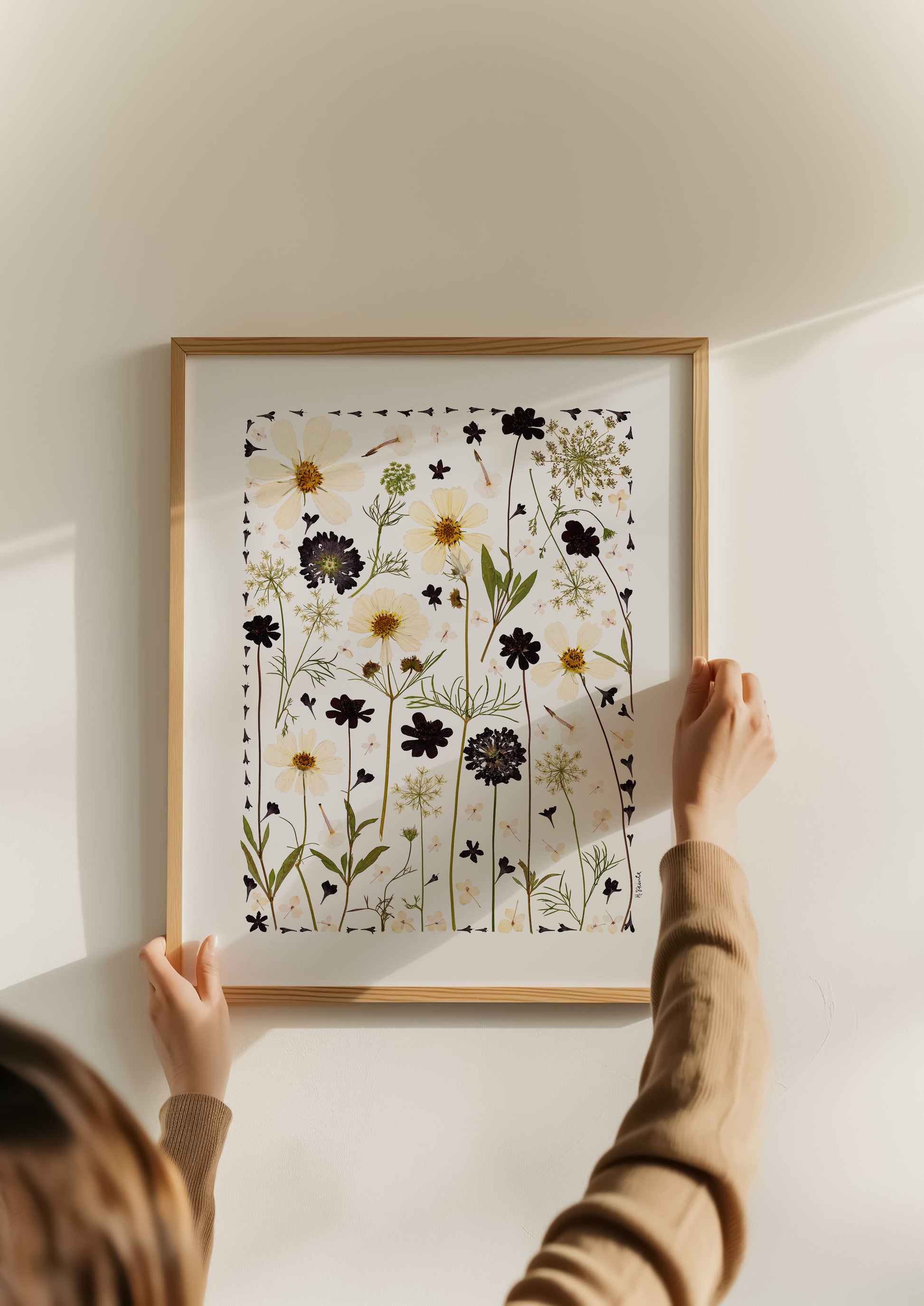 Person hanging a framed print of floral pressed flower collage art print design on a wall
