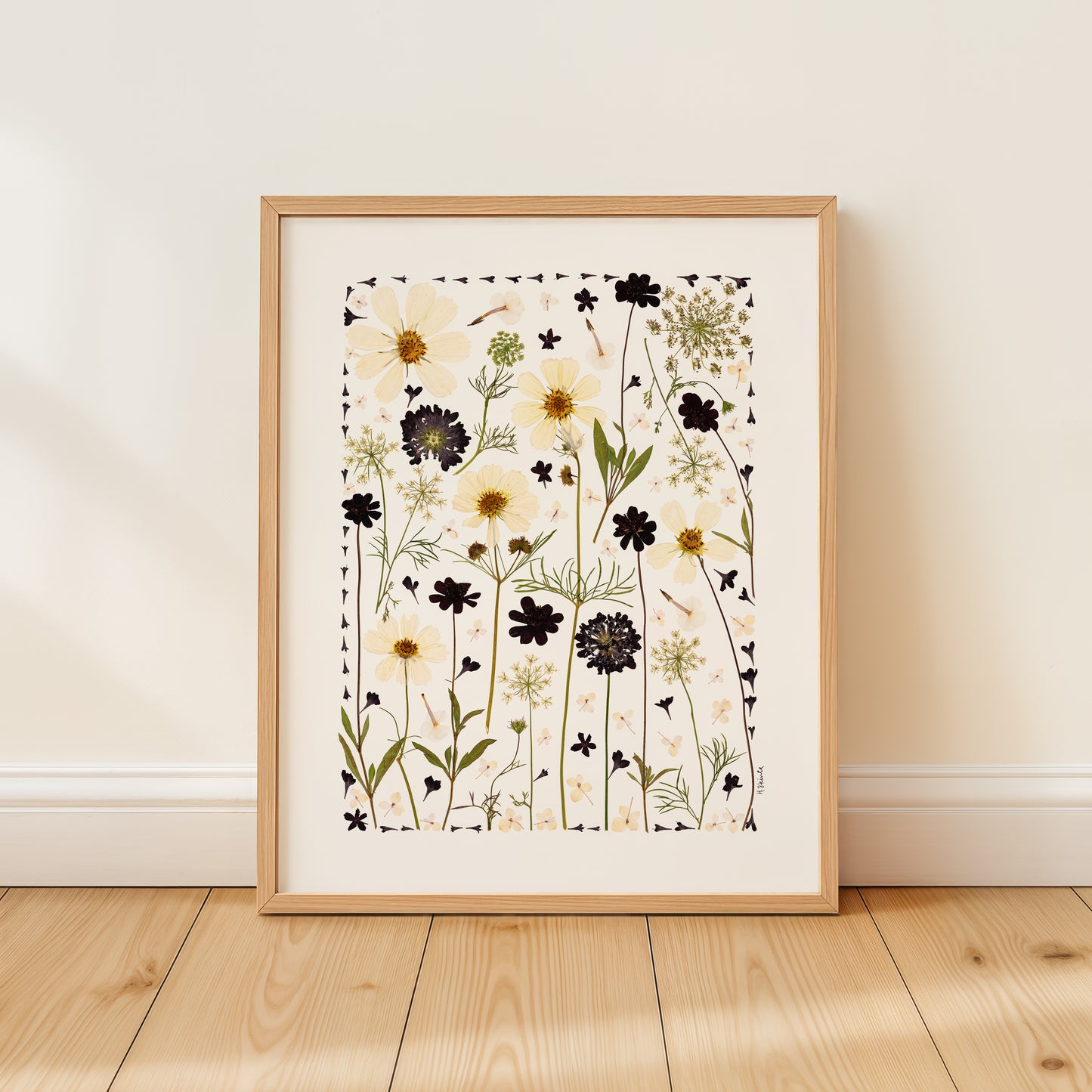 Framed floral pressed flower collage art print on a wooden floor with a white wall background