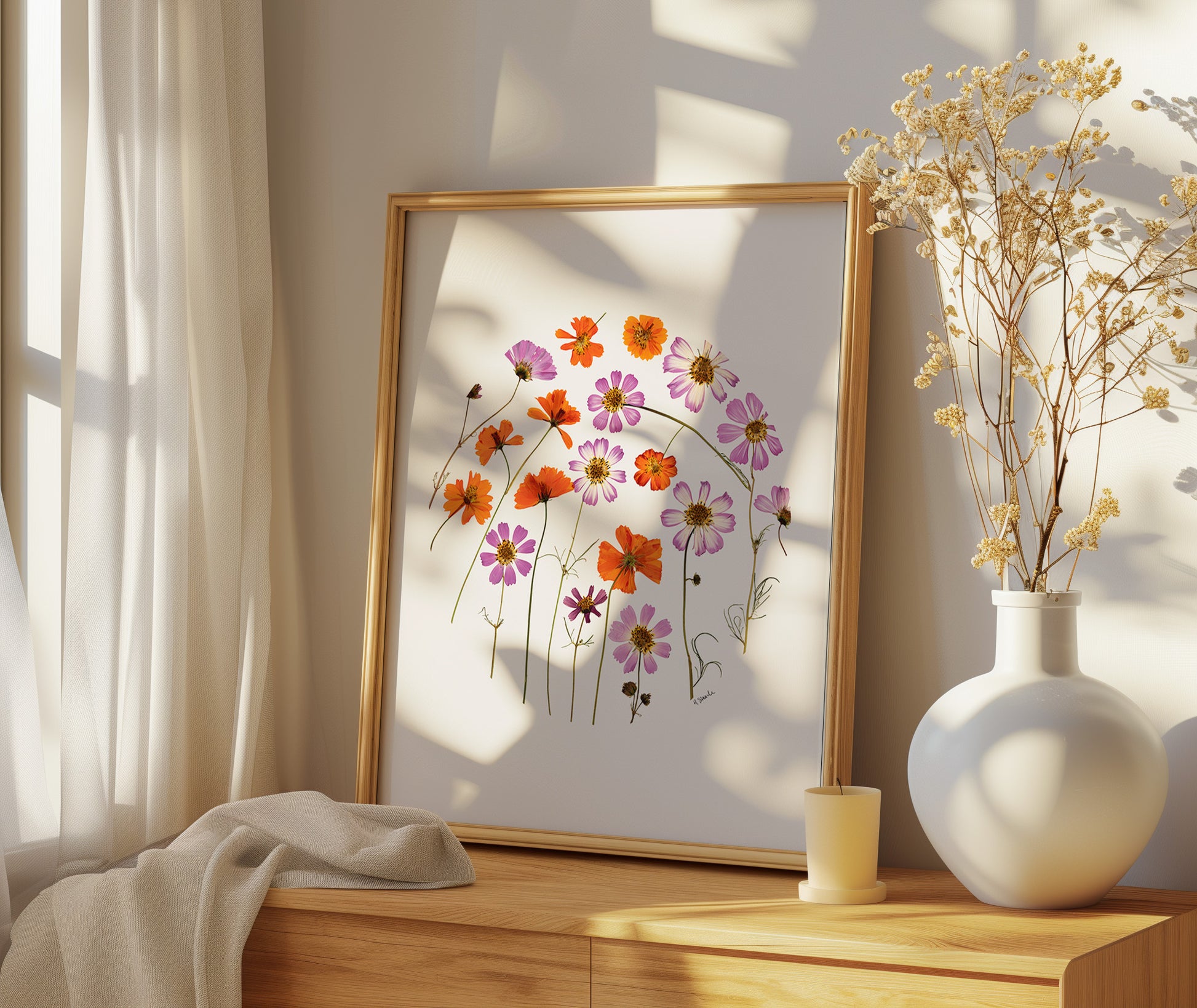 Framed floral pressed flower art print of cosmos on a wooden surface with a vase of dried flowers.