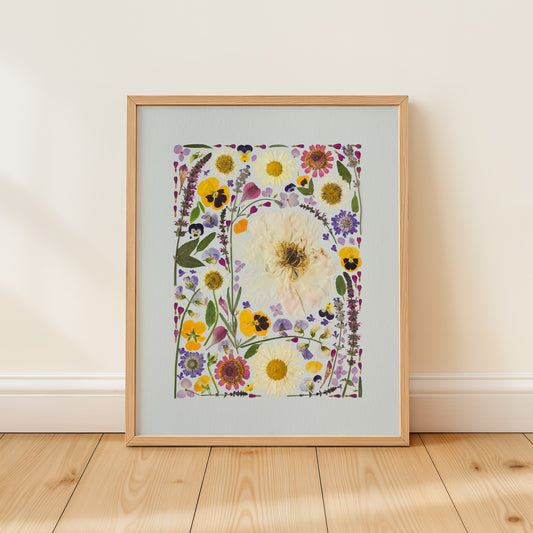 Framed fine art print of pressed flower collage on a light wooden floor and white wall background