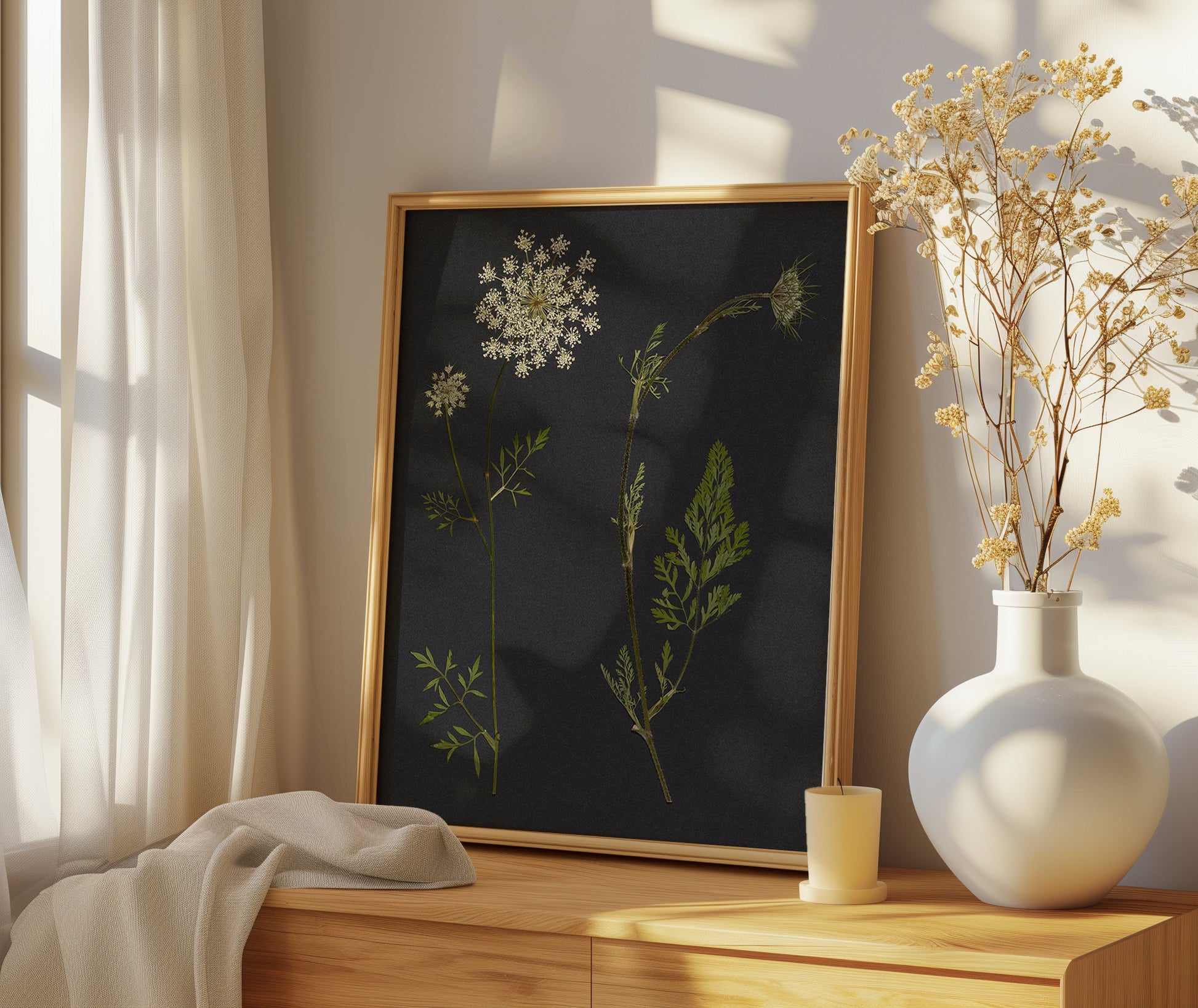 Framed botanical pressed flower art print on a wooden surface with a vase of dried flowers.