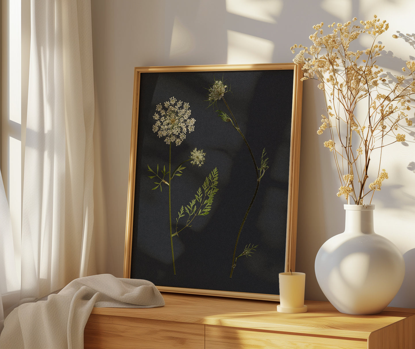 Framed floral pressed queen anne's lace art print on a wooden surface with a vase of dried flowers.