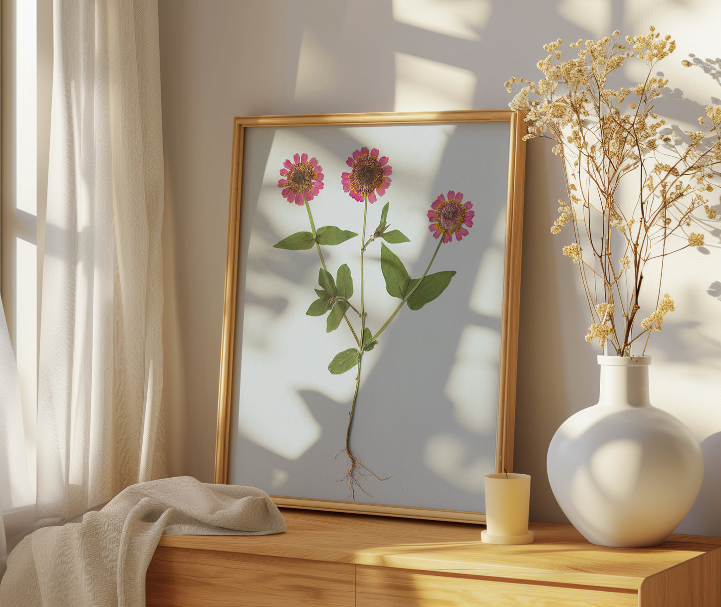 Framed botanical pressed zinnia with roots art print on a wooden surface with a vase of dried flowers.