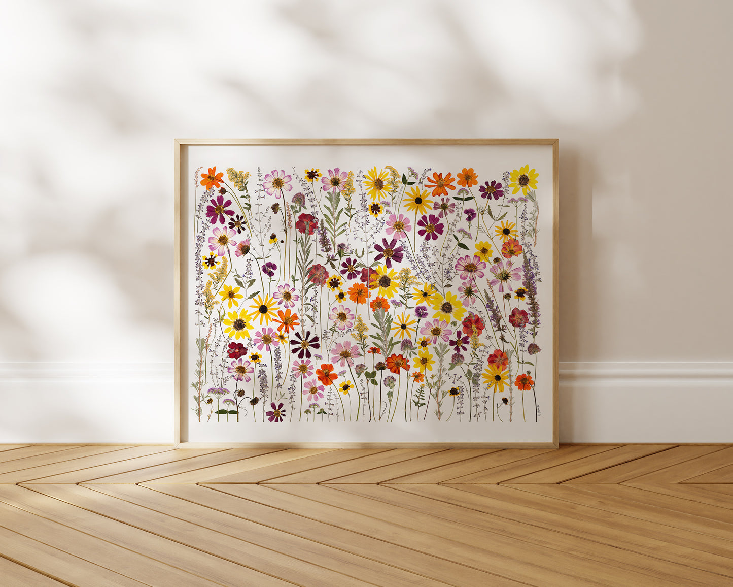 Framed pressed wildflowerflower art collage against a wall with wooden floor