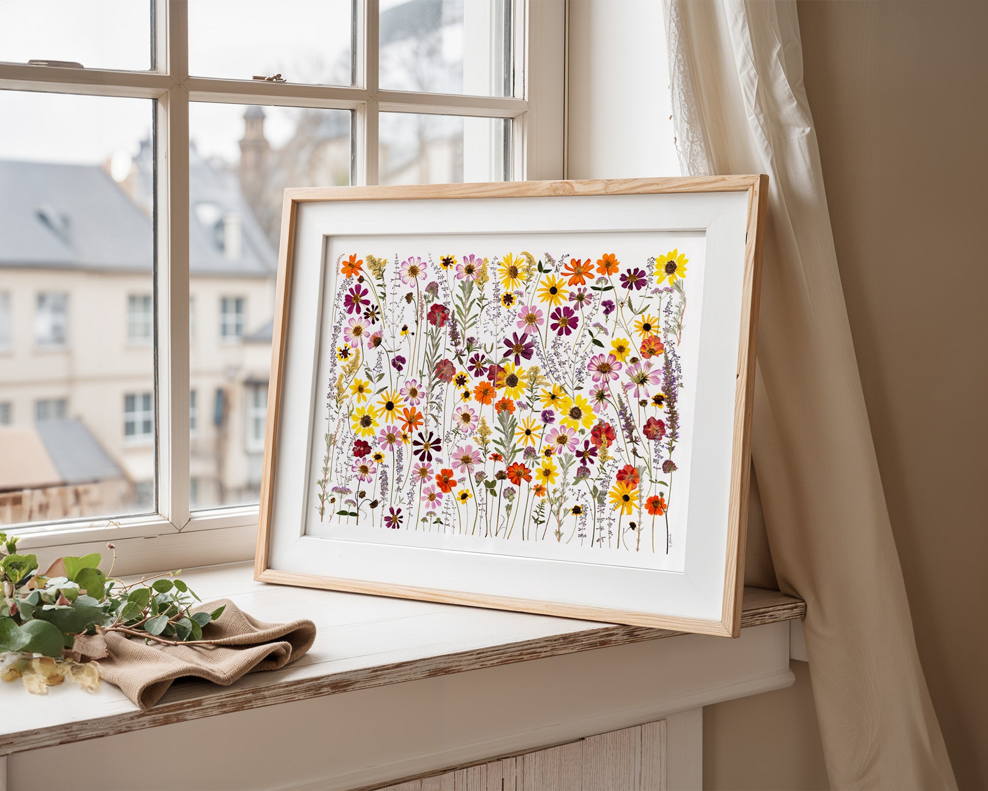 Framed pressed floral art print framed on a windowsill with a view of buildings outside