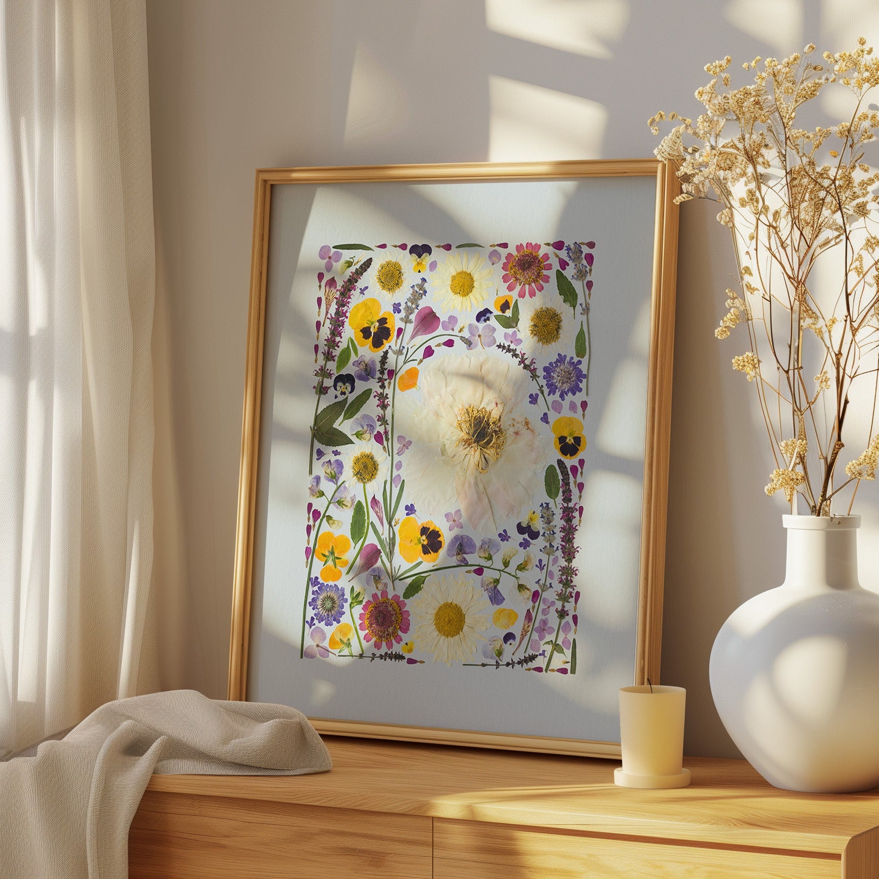 Framed floral artwork on a wooden surface with a vase of dried flowers.