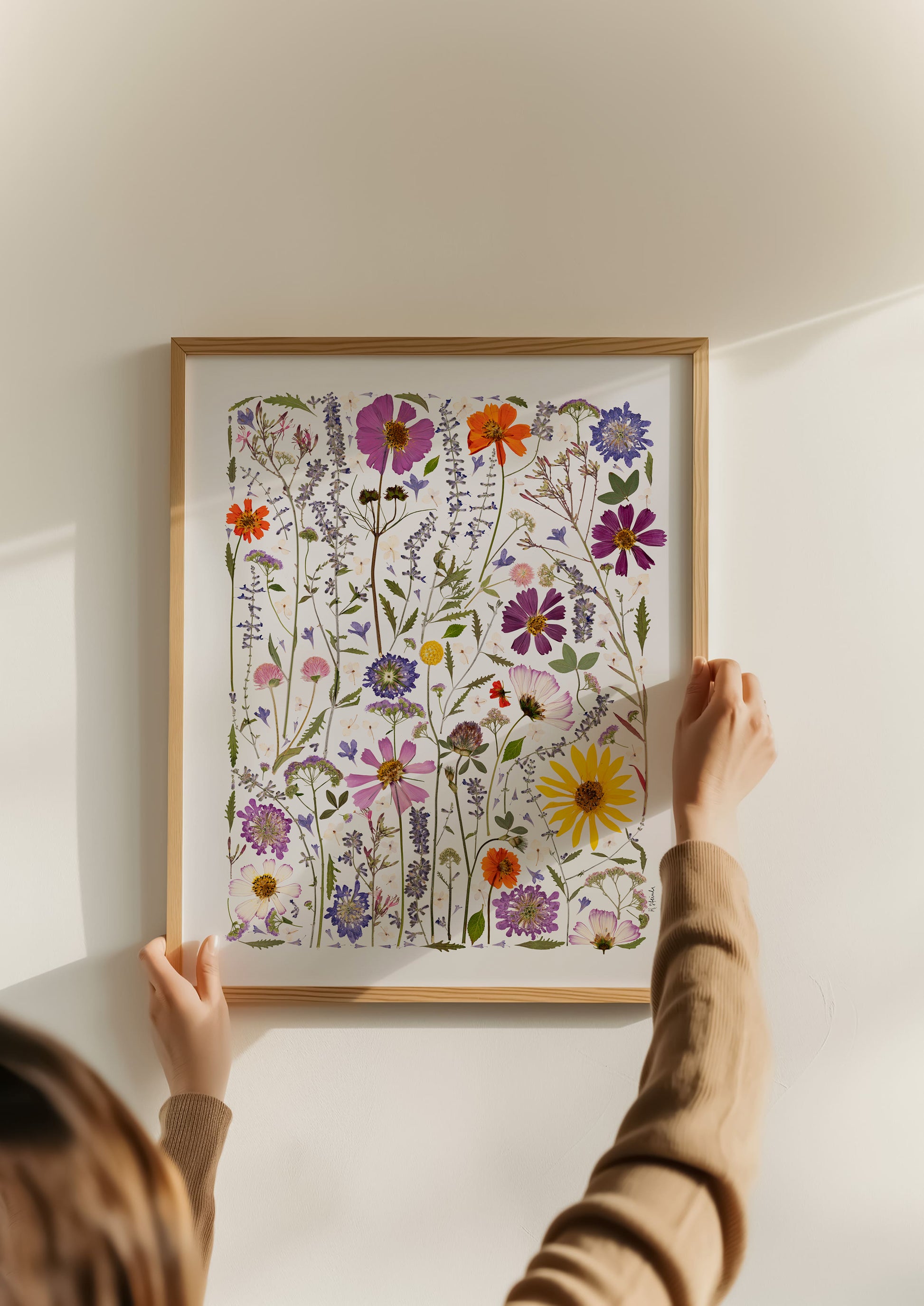 Person hanging a framed artwork of colorful flowers on a wall