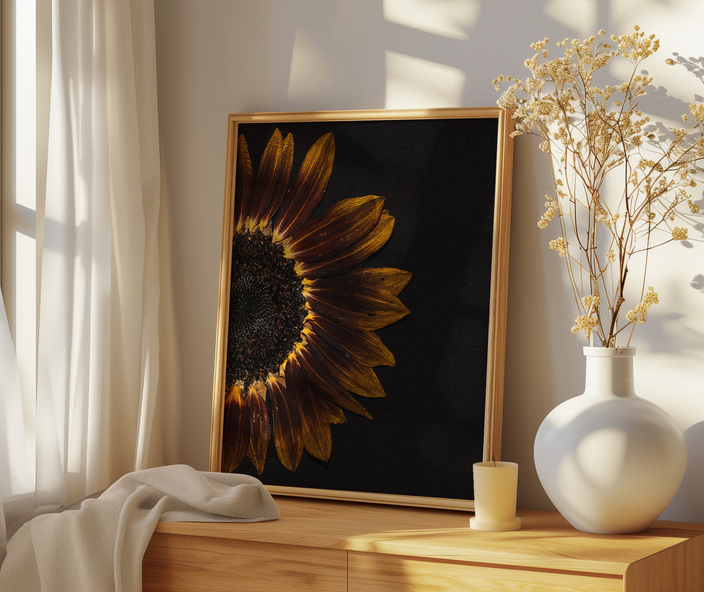 Framed pressed sunflower art print on a wooden surface with a vase of dried flowers.
